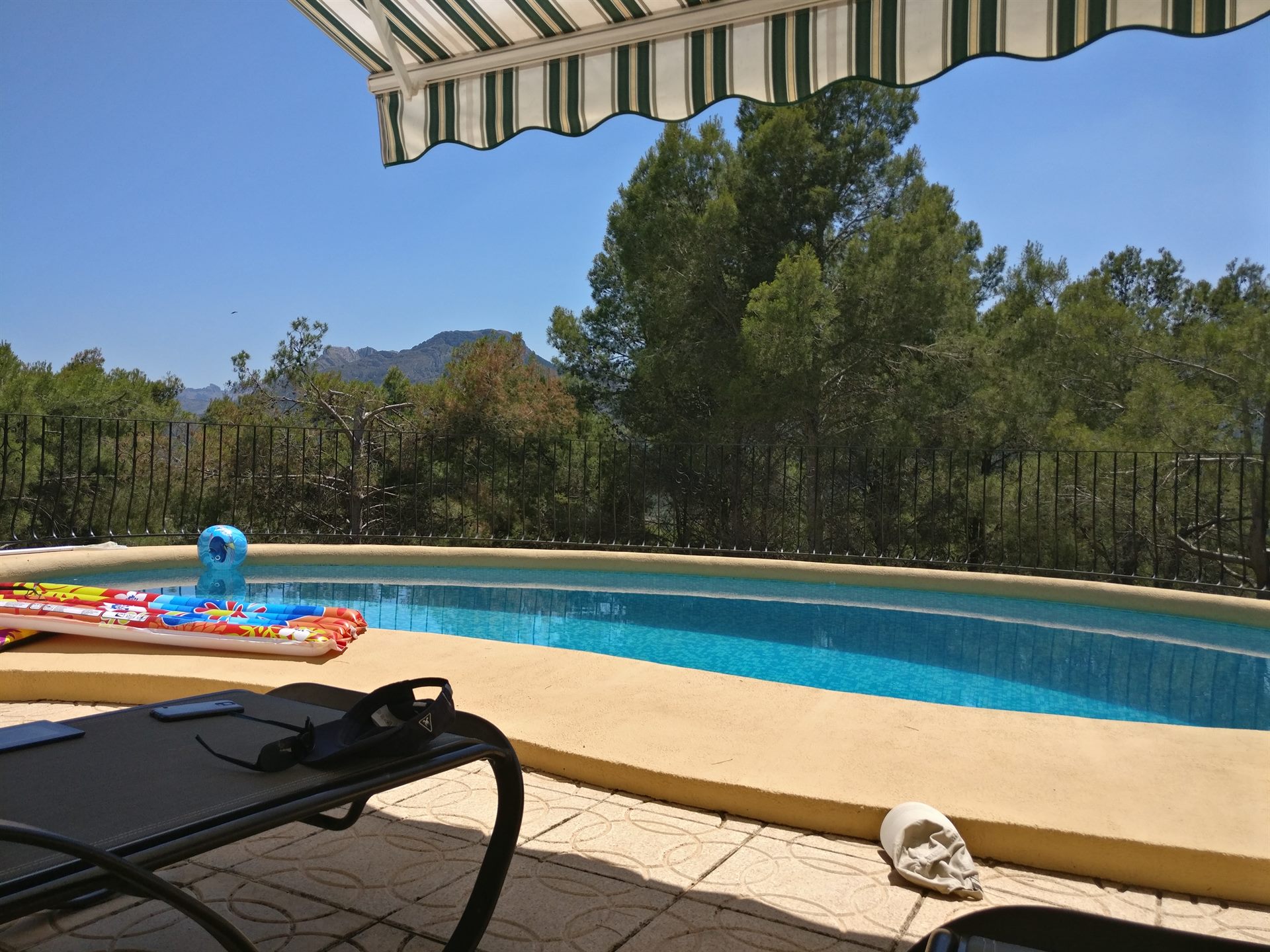 Piscina con colchonetas y una tumbona bajo un toldo, montañas al fondo