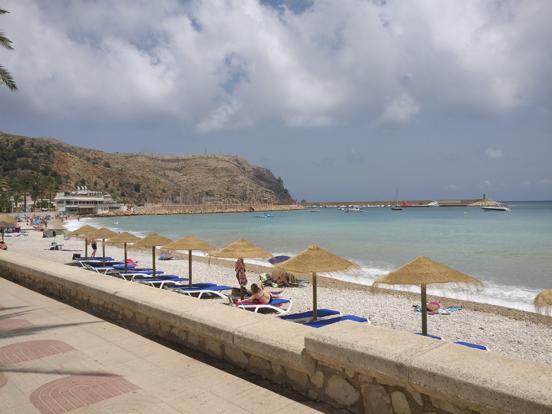 Sombrillas de paja y hamacas azules en la playa urbana de Jávea, justo al lado de los restaurantes del paseo