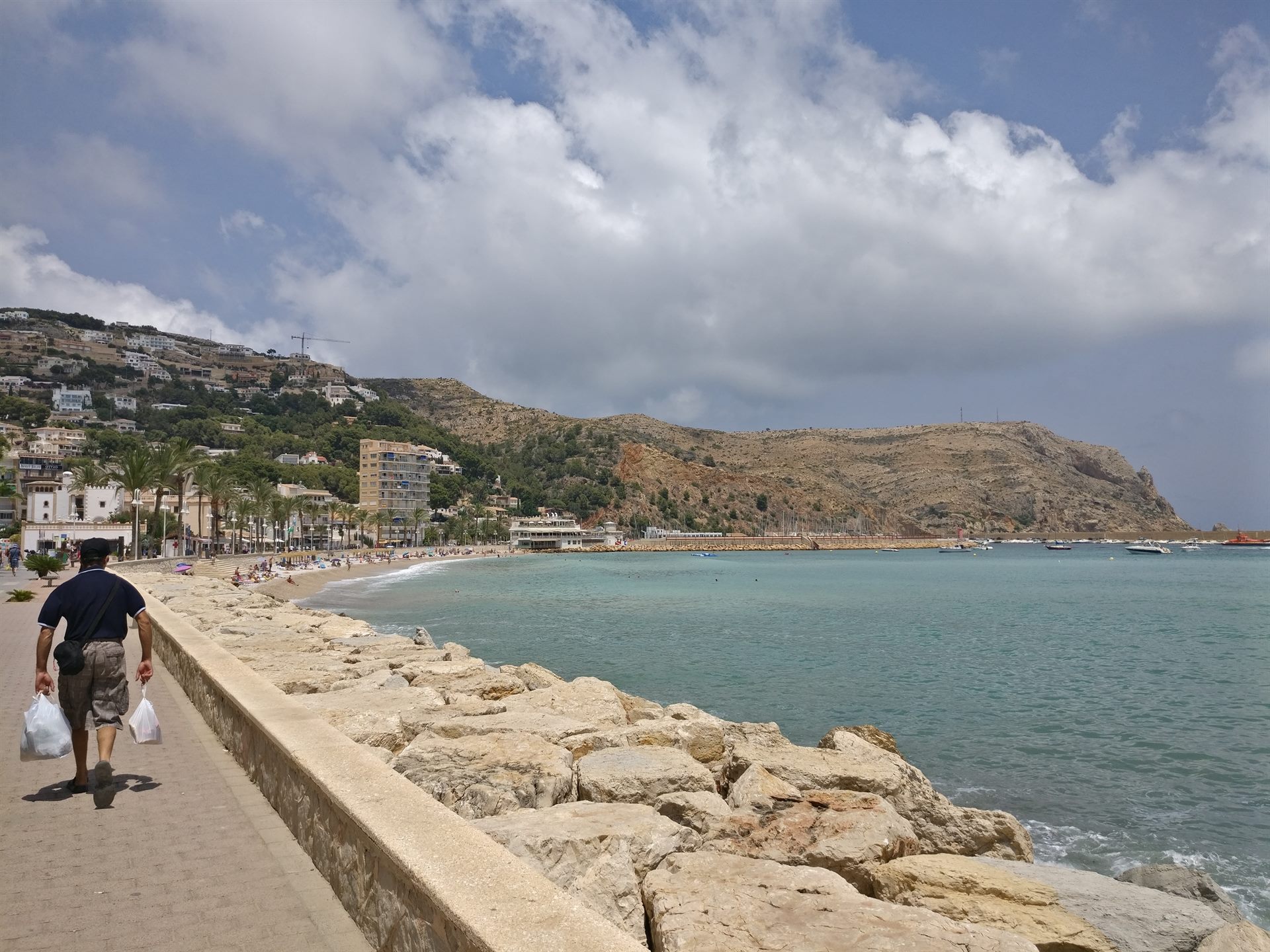 Paseo marítimo junto a la playa urbana de Jávea, con rocas en la orilla y un cabo al fondo