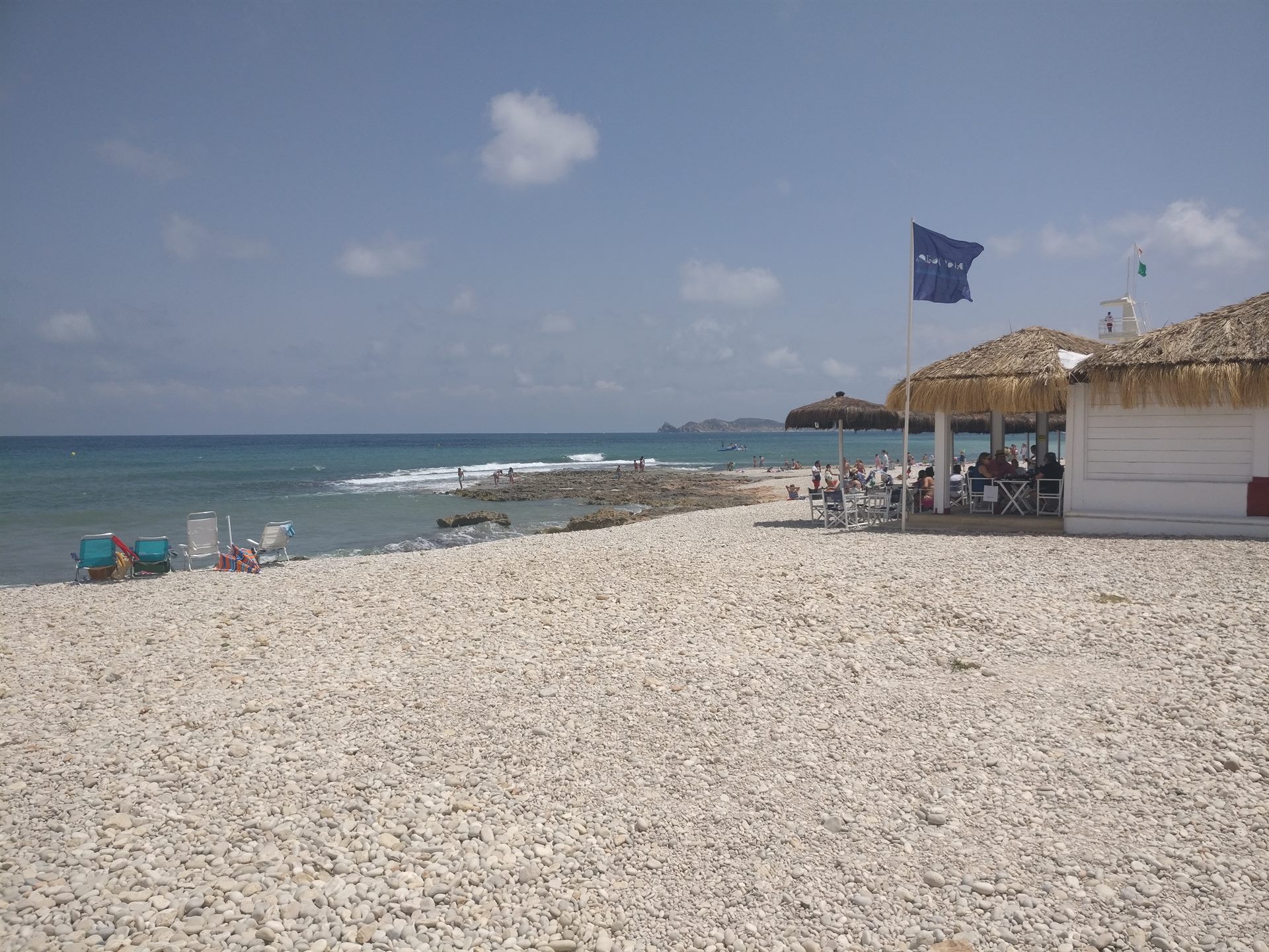 Playa de guijarros al sur de Jávea con un chiringuito de paja y la bandera azul