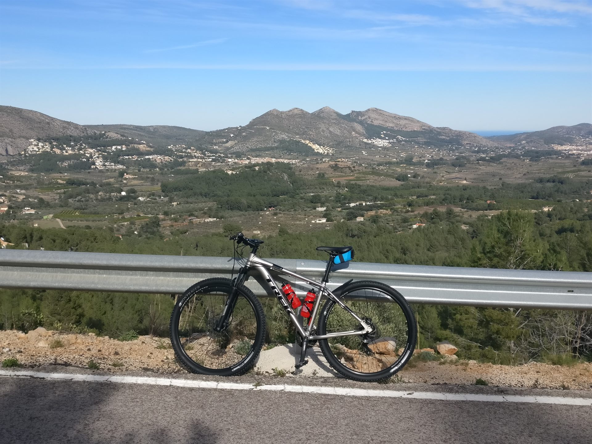 Mountain bike against the crash barrier on the Coll de Rates, with a view over the valley and the mountains towards the coast