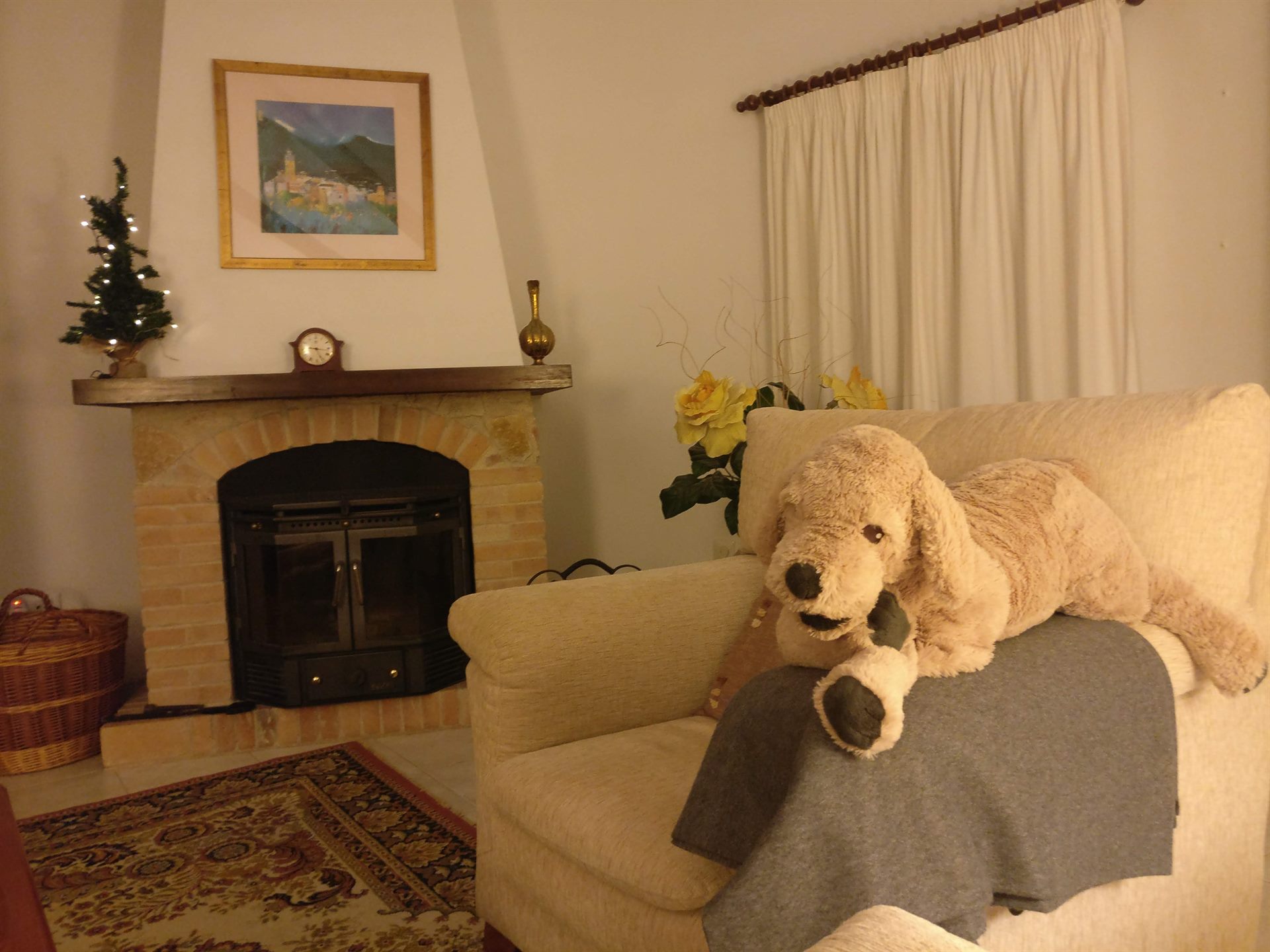 Sillón con un gran perro de peluche junto a la chimenea y un arbolito de Navidad iluminado
